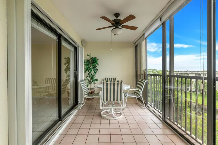Enclosed balcony featuring light-toned tile flooring, a ceiling fan with integrated lighting, and expansive sliding glass panels offering substantial natural light. Full accordion hurricane shutters.