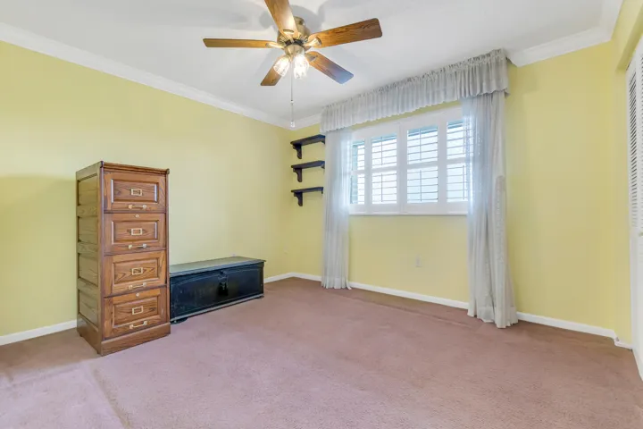 Carpeted room with a ceiling fan light fixture, crown molding, and a window featuring white plantation shutters and sheer lace curtains