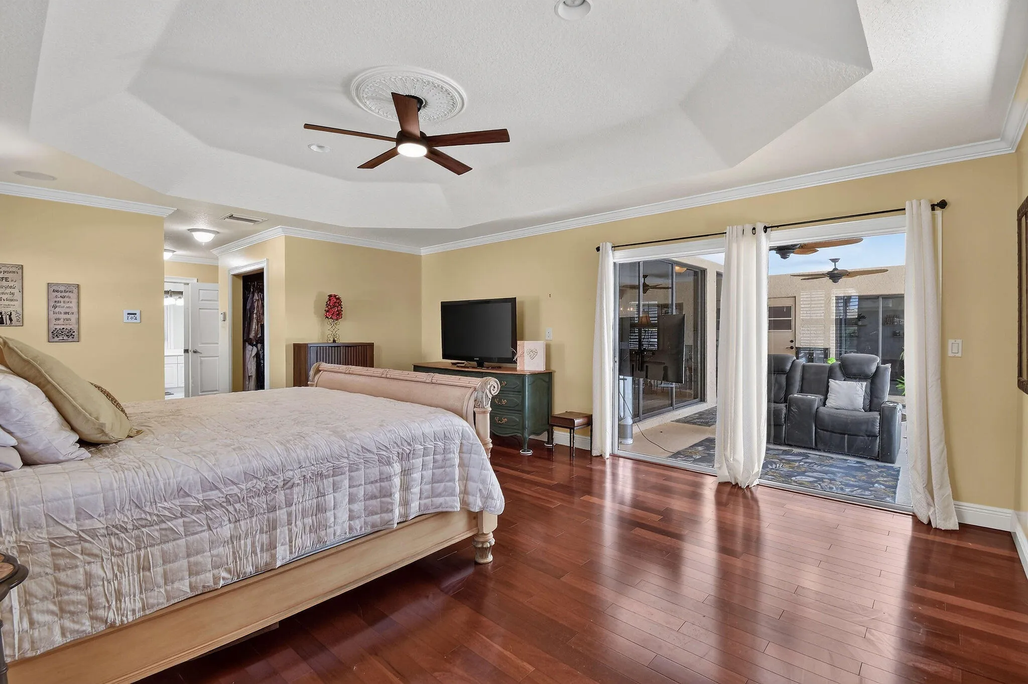 Primary bedroom with wood floors, tray ceiling, his and hers walk-in closets, and sliders to the screened/covered porch.