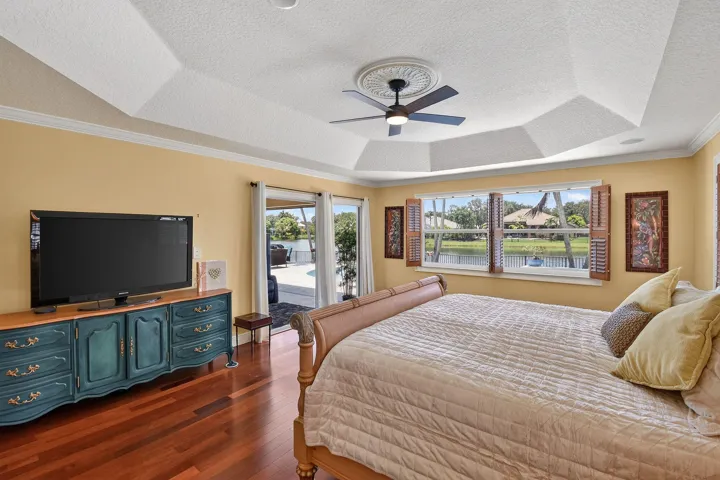 Primary bedroom with wood floors, tray ceiling, his and hers walk-in closets, and sliders to the screened/covered porch.