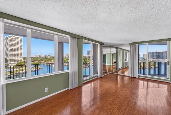 Floor-to-ceiling windows, wood-finish flooring, full-wall mirrors, and balcony access with water frontage