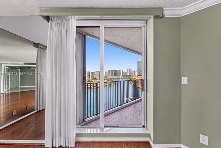 Floor-to-ceiling sliding glass doors opening to a private balcony with metal railing, wood-finish flooring, and wall-to-wall mirrored paneling