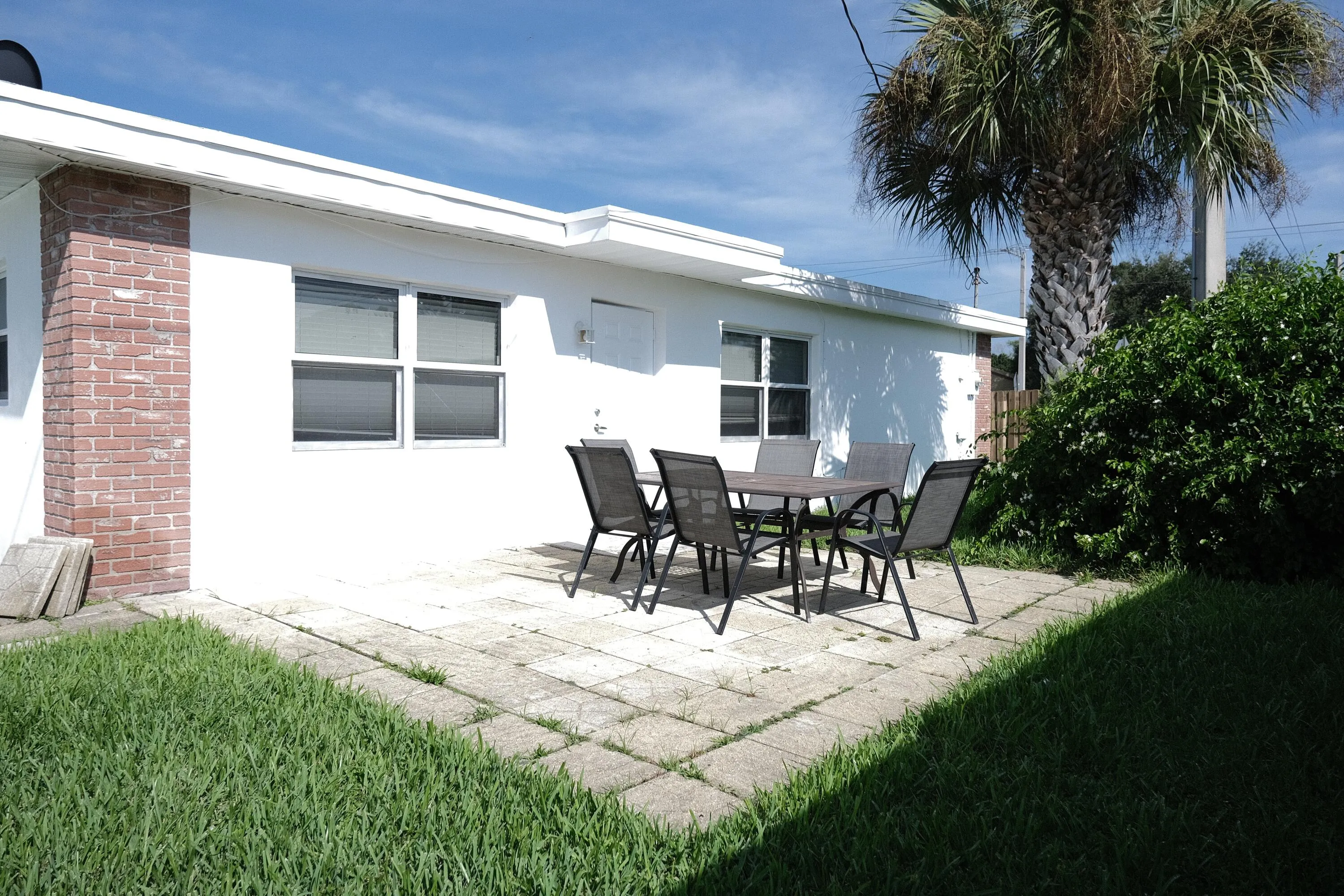 Exterior patio area featuring concrete pavers, a white stucco finish, and a red brick accent column