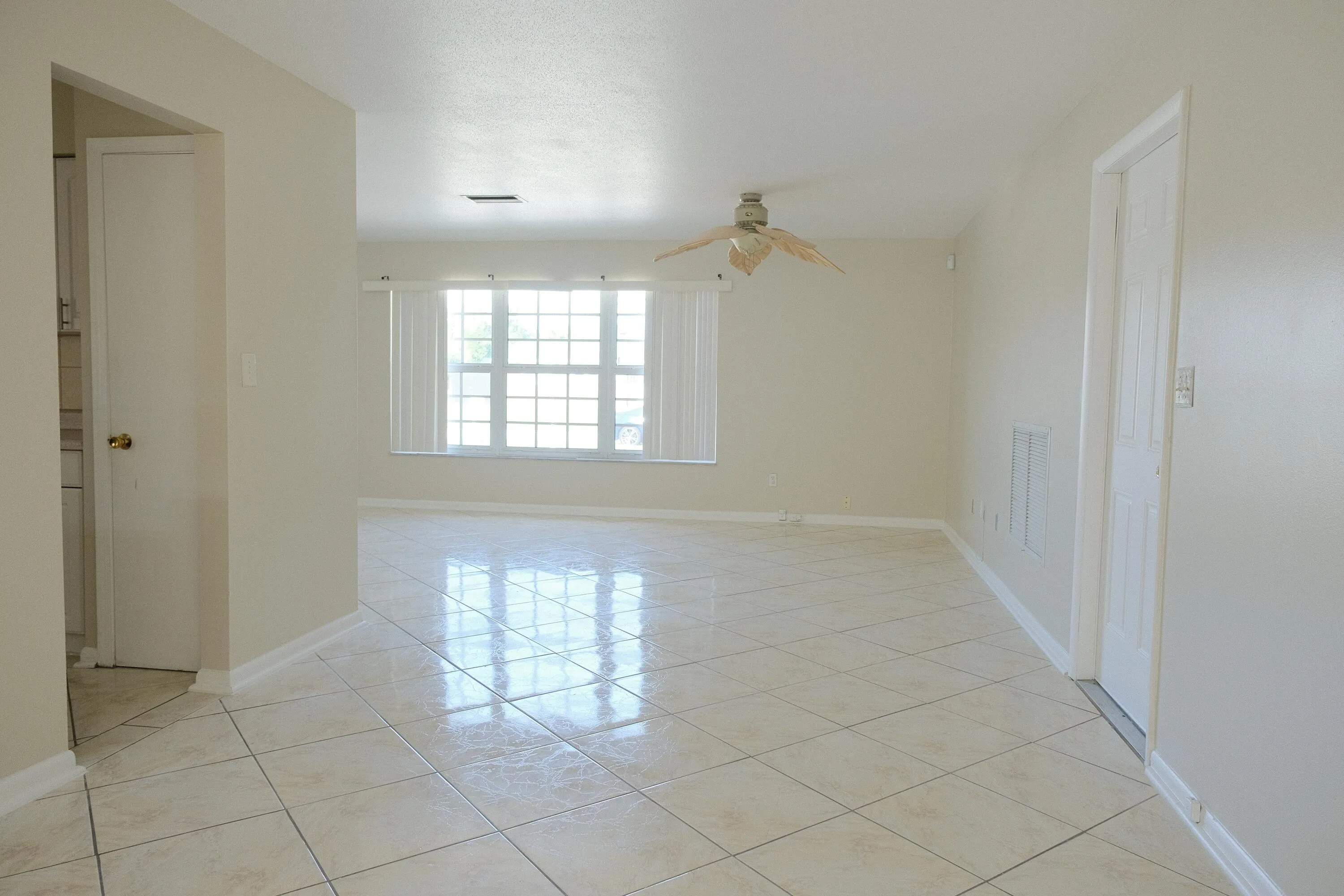 Spacious room featuring light-toned tile flooring, a multi-pane window with horizontal blinds, and a ceiling fan