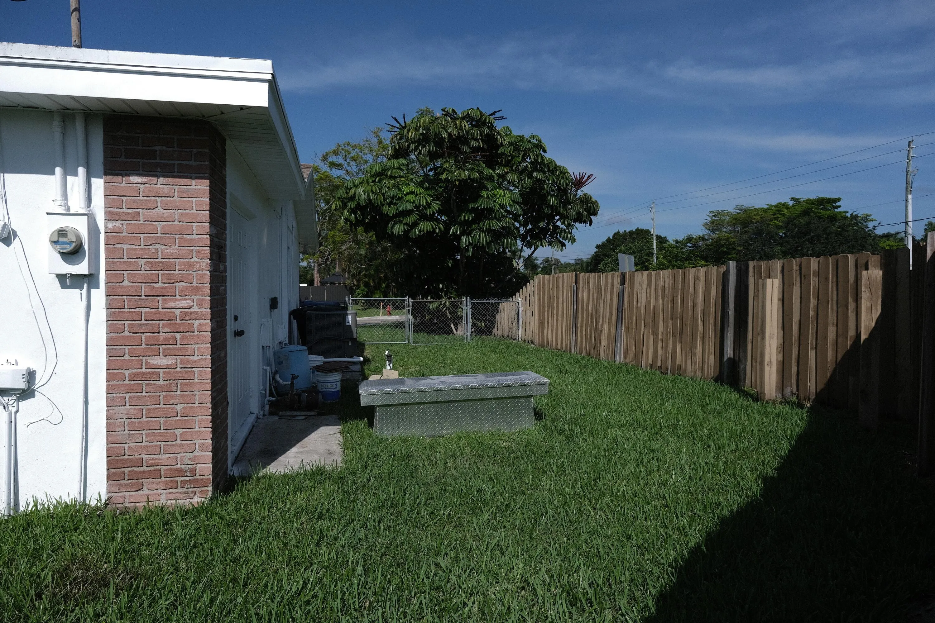 Expansive grassy backyard featuring a full privacy fence, mature landscaping, and a concrete patio area