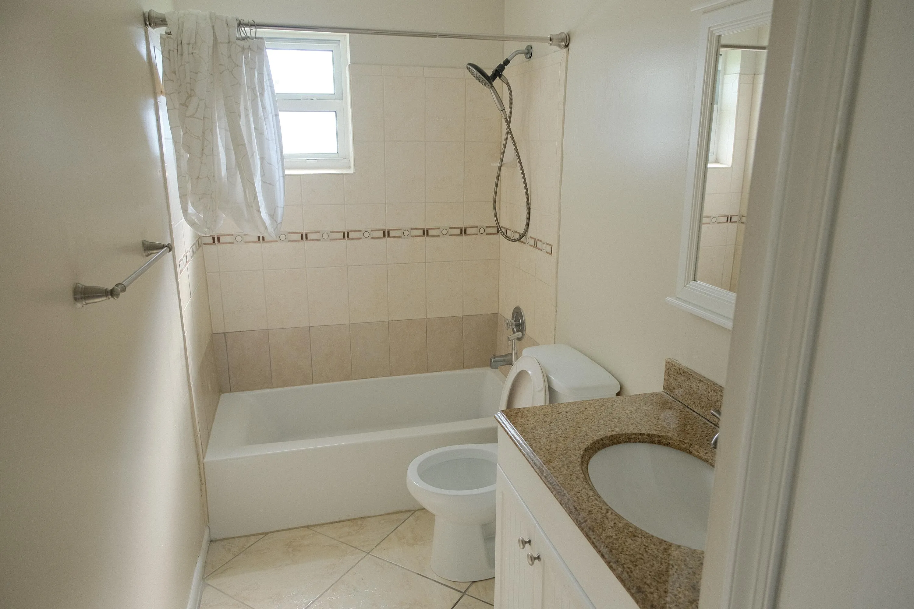 Bathroom featuring a white bathtub, ceramic tile surround with decorative accent band, and a vanity with a granite countertop
