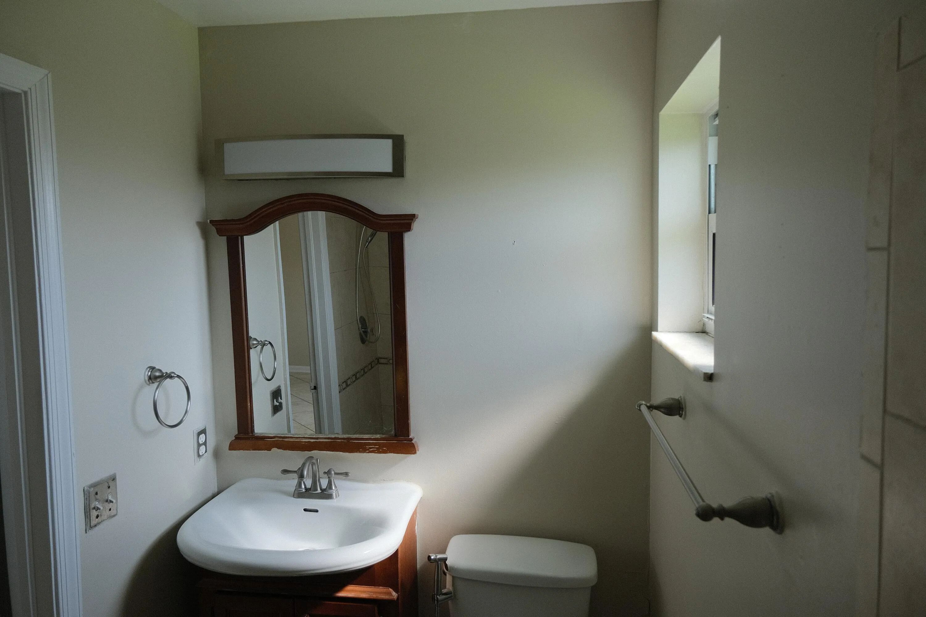 Bathroom with a white toilet, built-in window, and a vanity featuring a white sink, chrome faucet, and wood-framed mirror with overhead lighting