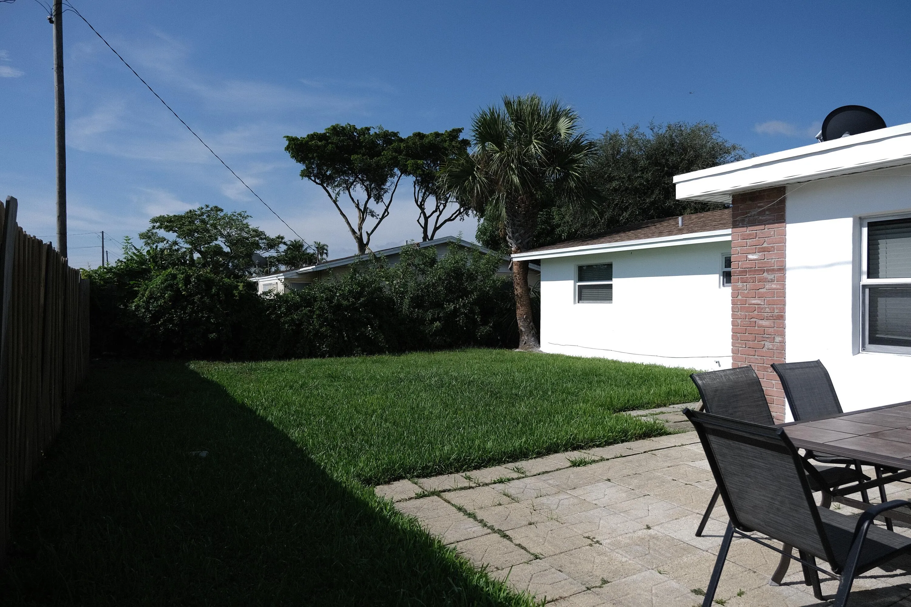 Expansive grassy yard area with a paved patio, partial privacy fencing, and mature landscaping