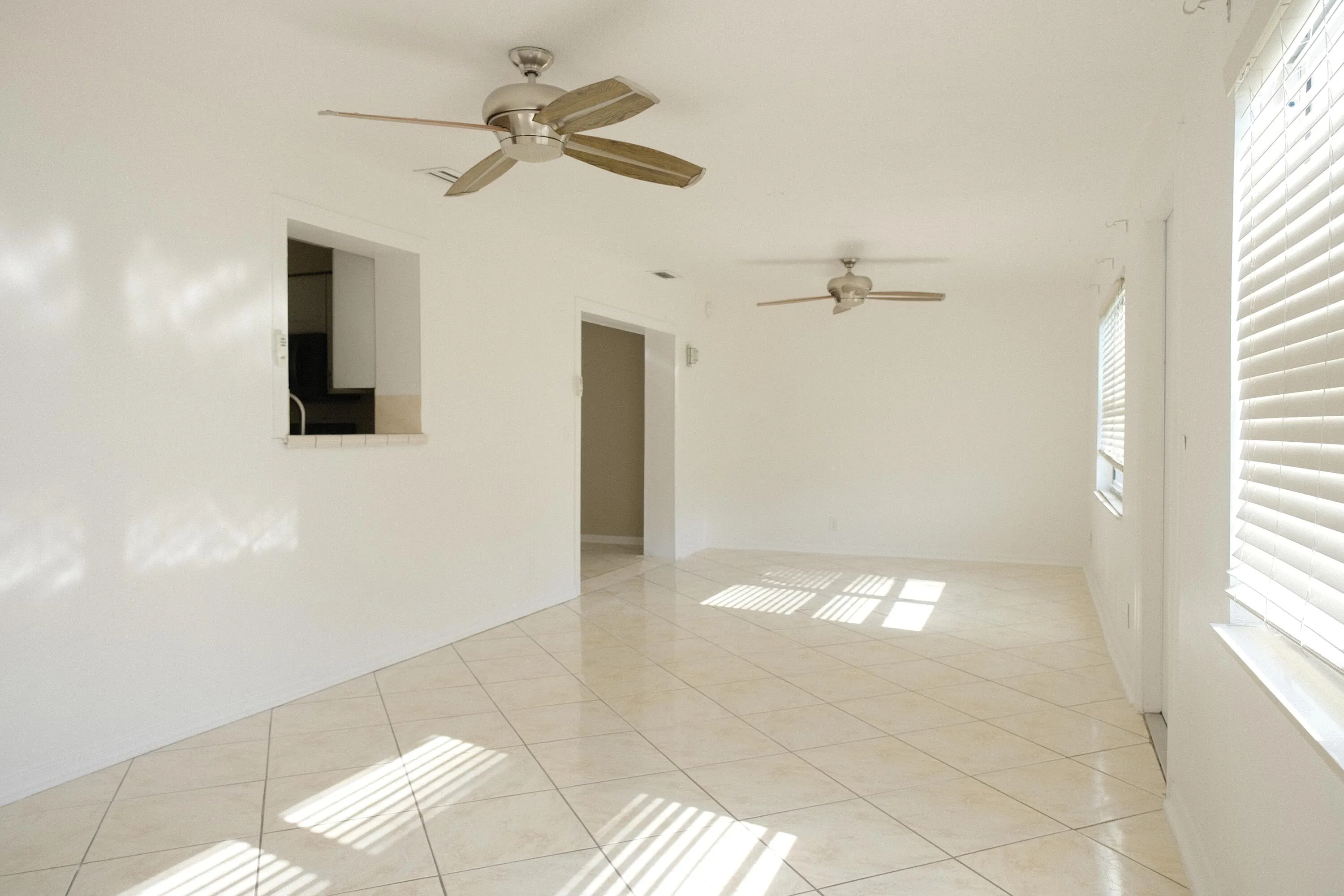 Spacious room featuring light-toned tile flooring and multiple windows with horizontal blinds