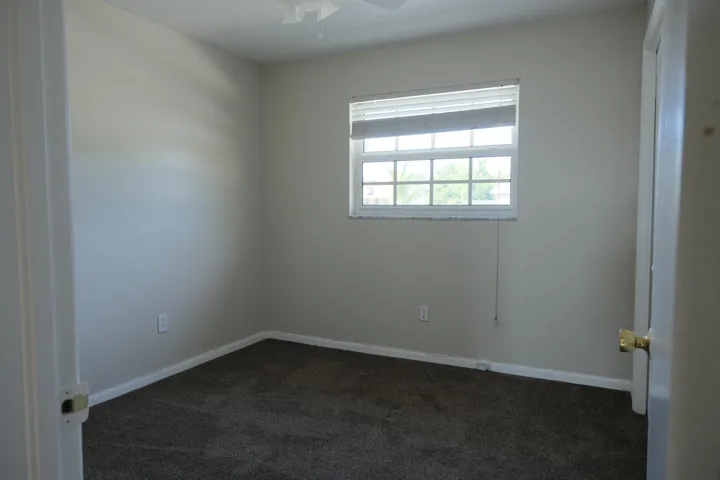 Carpeted interior room featuring light neutral wall tones, white trim, and a window with horizontal blinds
