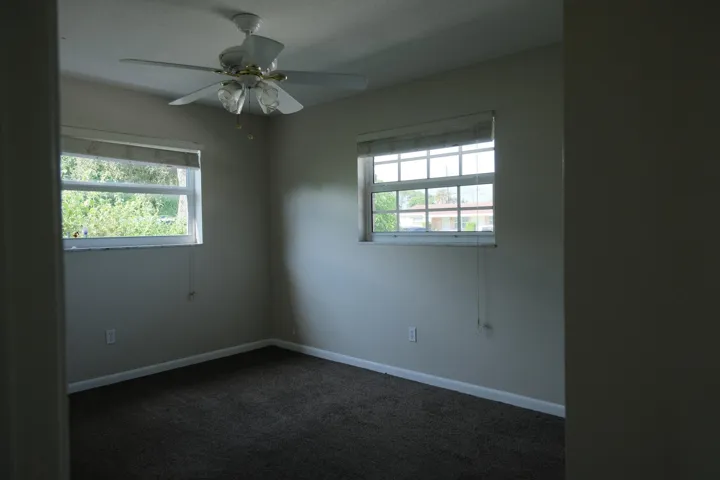 Carpeted room featuring two windows with horizontal blinds, a ceiling fan with light kit, and white baseboards