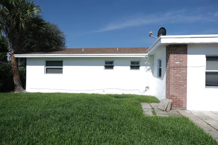 White stucco exterior with a brown shingle roof, complemented by a red brick accent wall