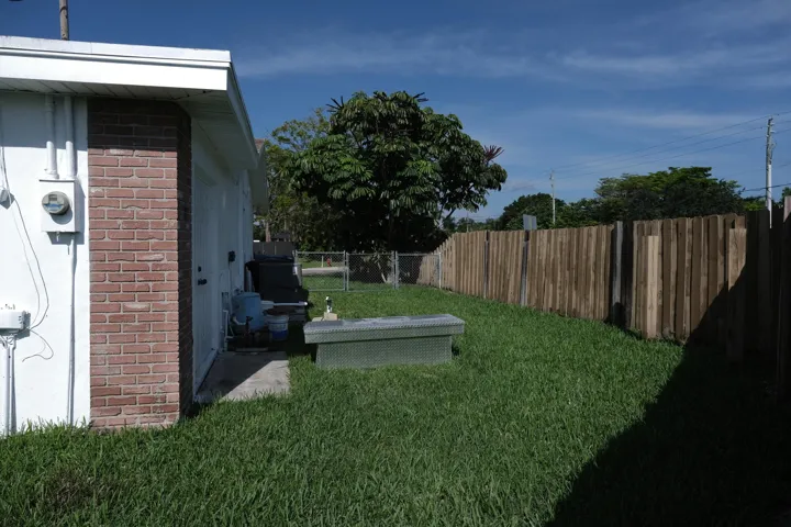Expansive grassy backyard featuring a full privacy fence, mature landscaping, and a concrete patio area