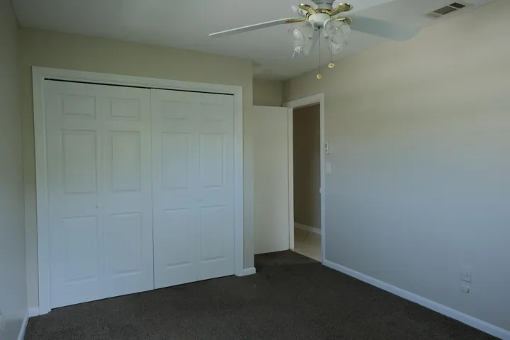 Neutral-toned room featuring a four-panel bi-fold closet, ceiling fan with integrated lighting, and carpet flooring