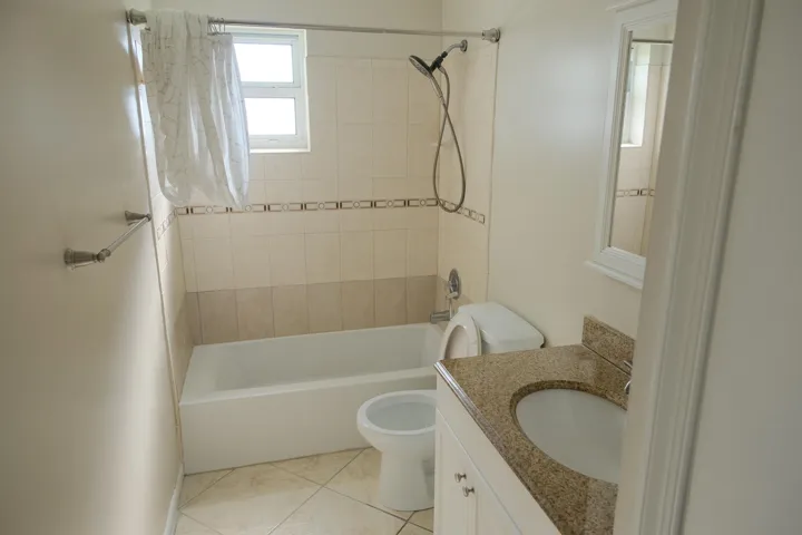 Bathroom featuring a white bathtub, ceramic tile surround with decorative accent band, and a vanity with a granite countertop