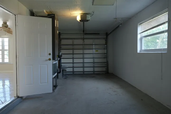Spacious garage featuring a concrete floor, overhead garage door with opener, and a window with blinds