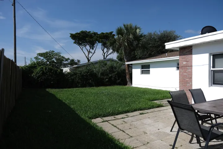 Expansive grassy yard area with a paved patio, partial privacy fencing, and mature landscaping