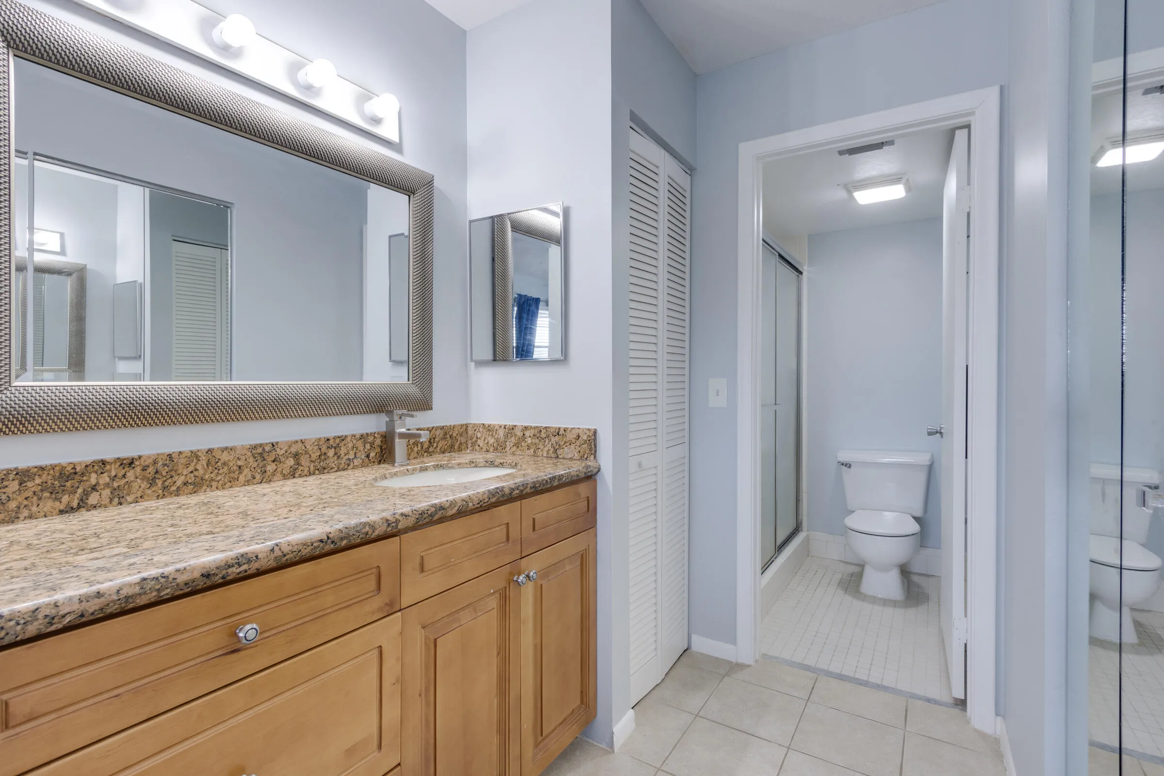 Large vanity with granite countertop, wood cabinetry, linen closet & walk-in shower.