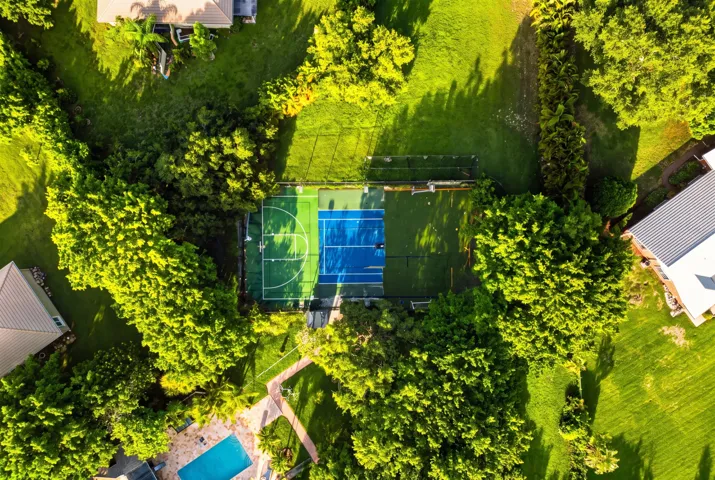 Multi-sport court featuring blue and green playing surfaces, surrounded by mature trees and lush green landscaping