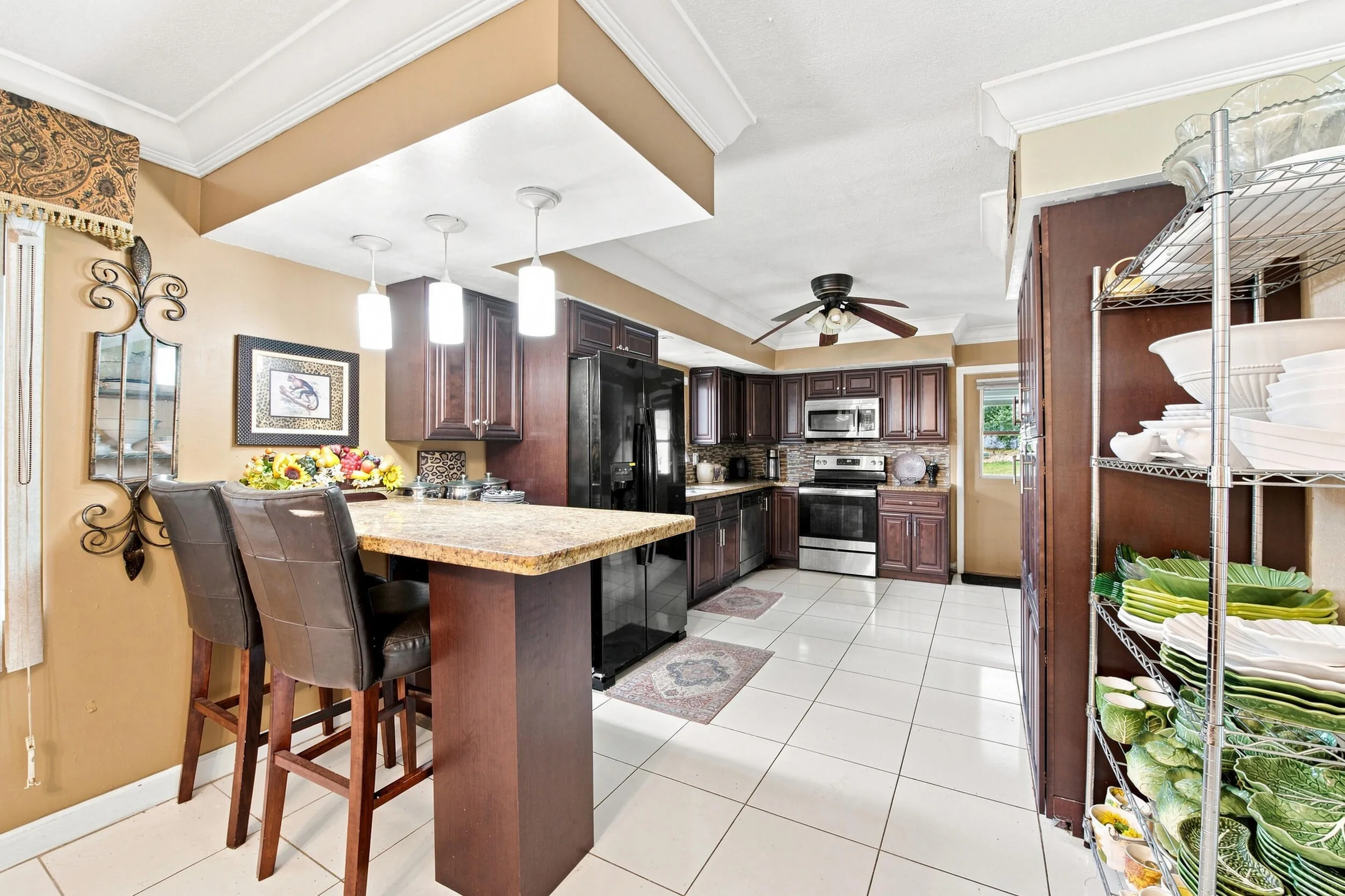 Kitchen featuring an island with stone-finish countertop and pendant lighting, dark wood-finish cabinetry, stainless steel appliances, and white tile flooring