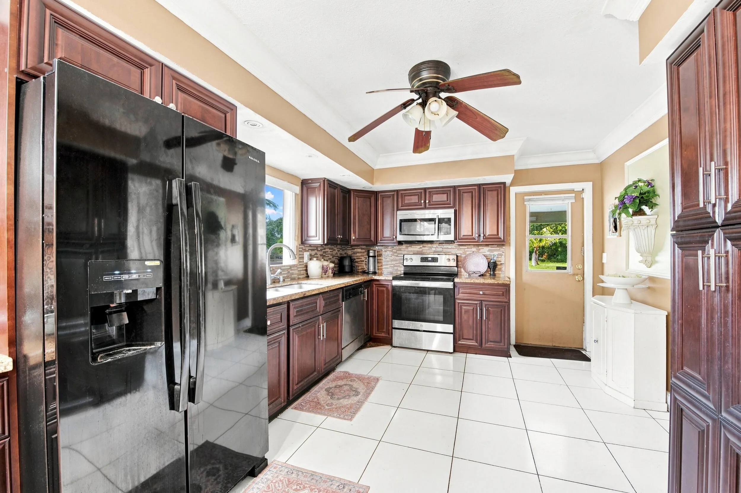 Kitchen featuring dark wood cabinetry, stainless steel appliances, white tile flooring, and a ceiling fan