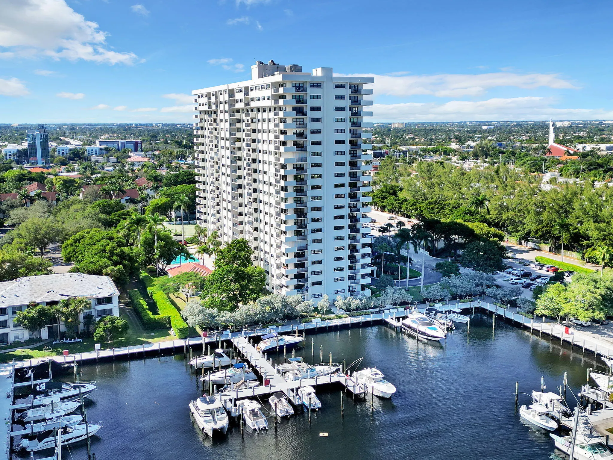 High-rise residential building featuring multiple private balconies, an onsite marina with numerous boat slips, a terraced swimming pool, and extensive landscaping