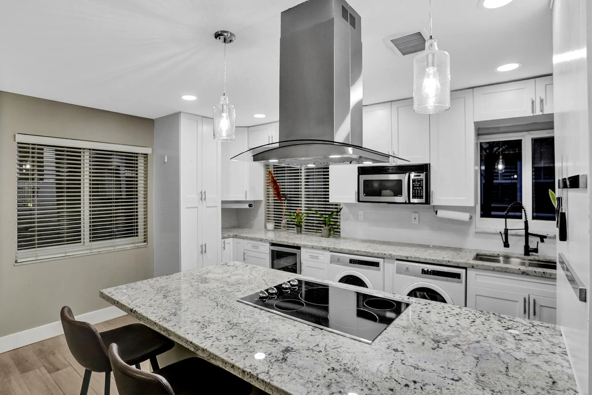 Modern kitchen featuring white shaker cabinetry, speckled countertops, stainless steel appliances, and a central island with an integrated cooktop