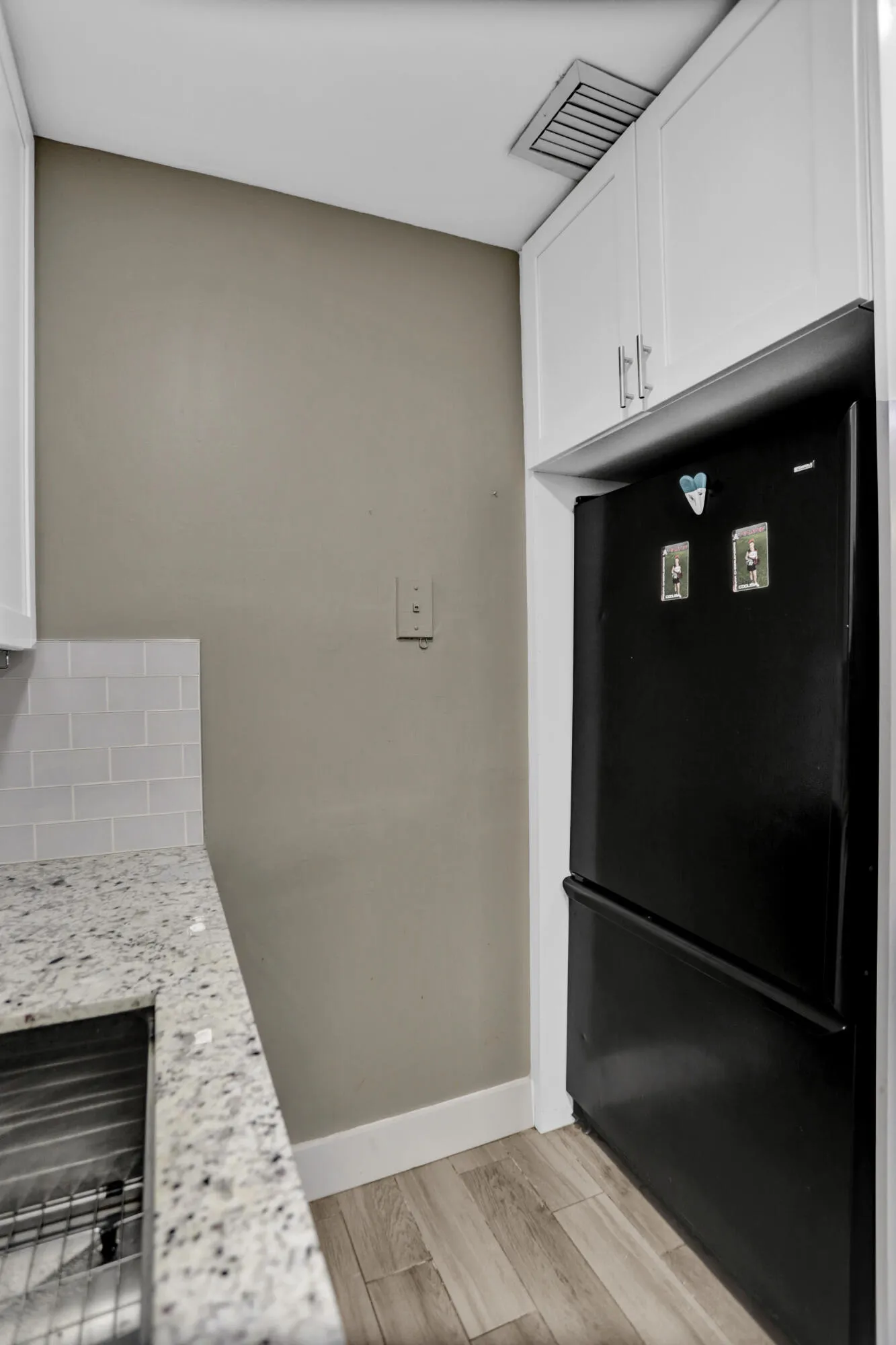 Updated kitchen featuring white shaker cabinetry, speckled countertop, tile backsplash, stainless steel sink, and wood-finish flooring