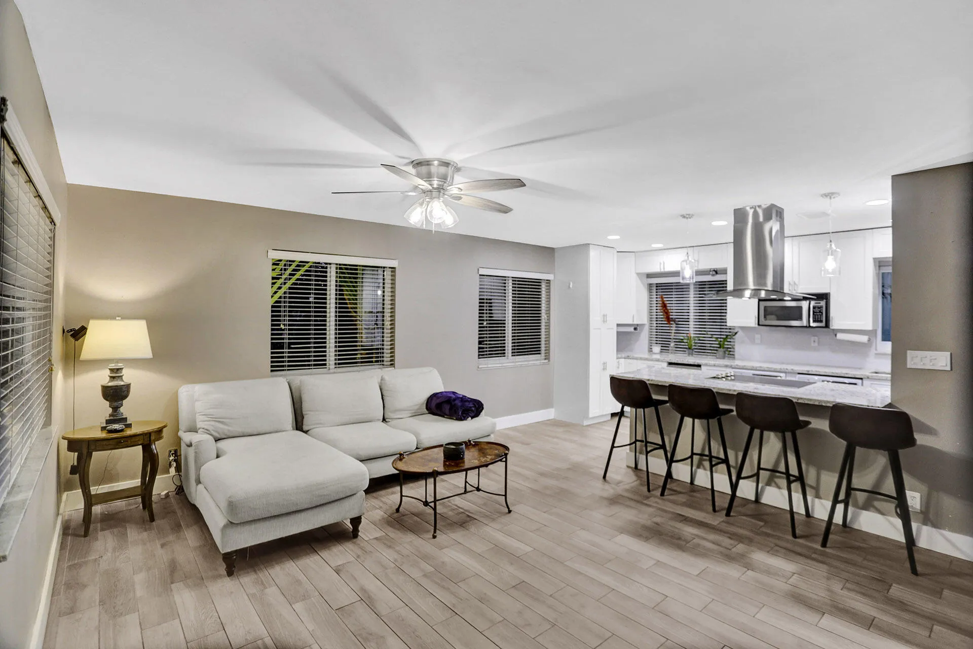 Open-concept living area featuring wood-finish flooring, a contemporary ceiling fan, and multiple windows