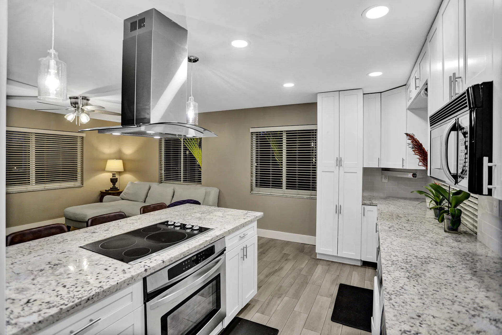 Open-concept kitchen featuring an island with an integrated cooktop and stainless steel oven, white cabinetry, speckled countertops, and recessed lighting