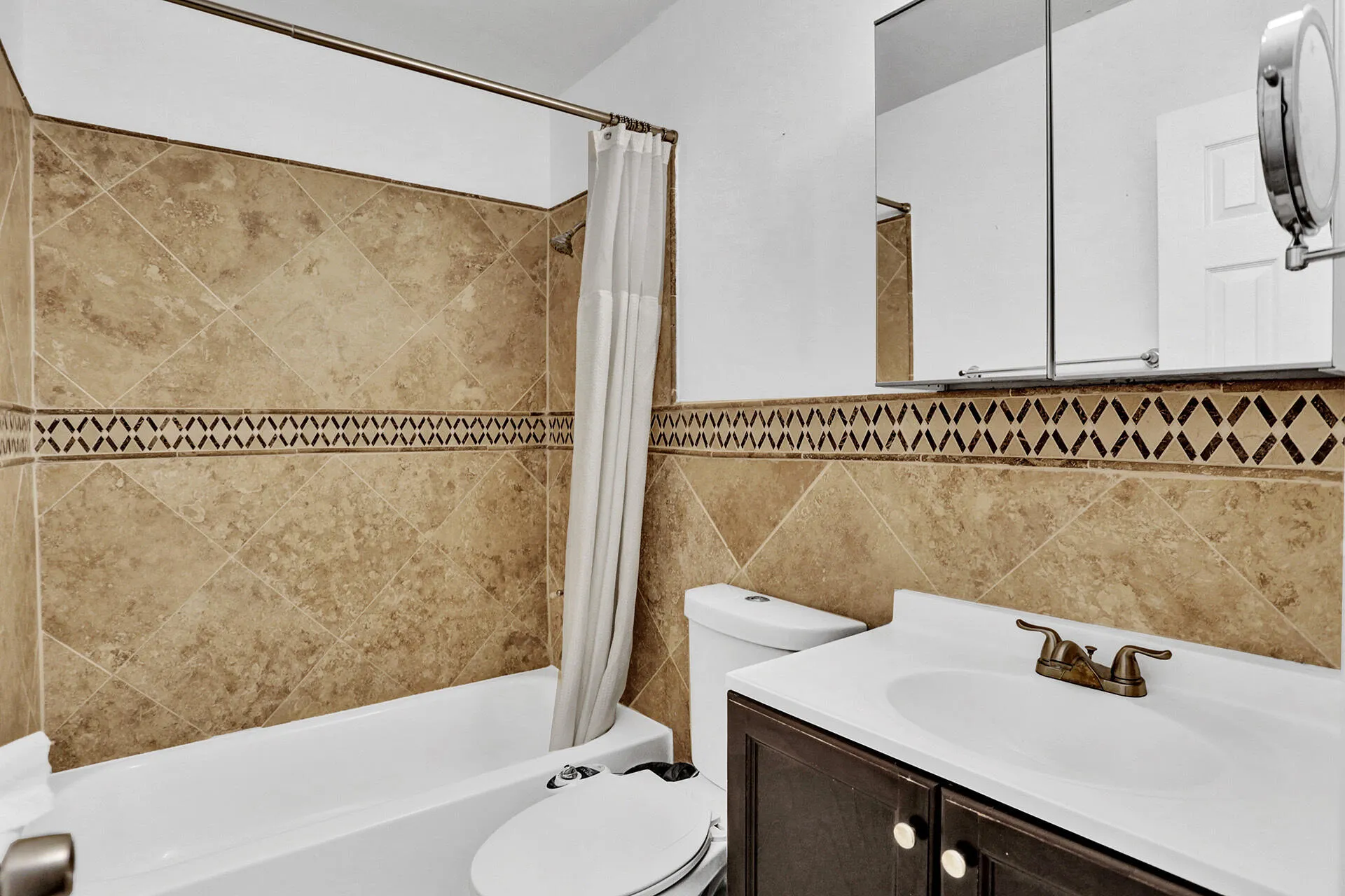 Full bathroom featuring a tub/shower combination with natural-tone tile surround and decorative accent banding