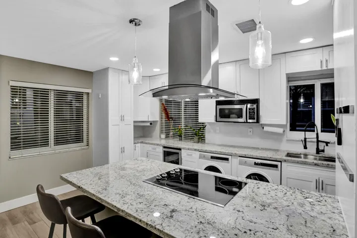 Modern kitchen featuring white shaker cabinetry, speckled countertops, stainless steel appliances, and a central island with an integrated cooktop