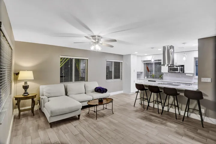 Open-concept living area featuring wood-finish flooring, a contemporary ceiling fan, and multiple windows