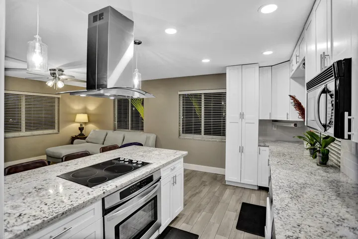 Open-concept kitchen featuring an island with an integrated cooktop and stainless steel oven, white cabinetry, speckled countertops, and recessed lighting