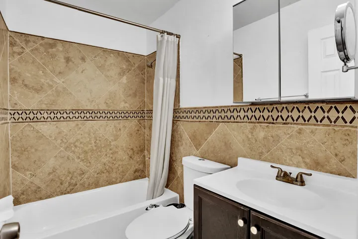 Full bathroom featuring a tub/shower combination with natural-tone tile surround and decorative accent banding