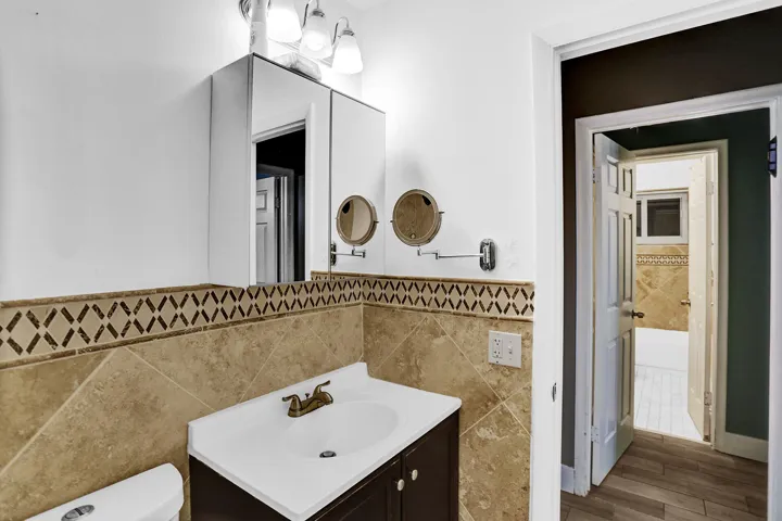 Bathroom vanity with a white countertop and integrated sink, set against a tiled backsplash featuring a decorative accent border