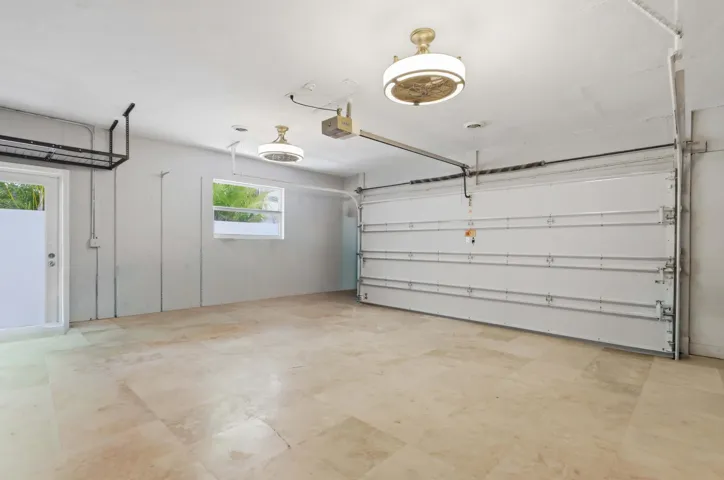 Spacious garage featuring light-toned tile flooring, overhead lighting, a white garage door, and an exterior access door with frosted glass