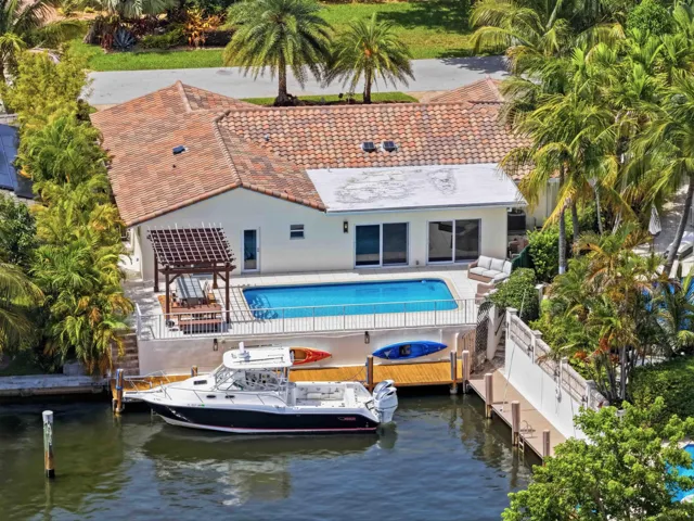 Waterfront residence with a private boat dock, featuring a pool deck, a pergola-covered patio, and a tile roof