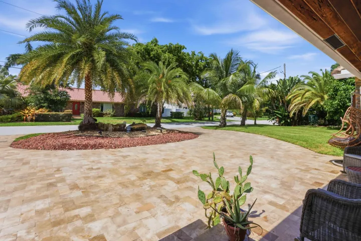 Expansive paver driveway with a central landscaped island featuring mature palm trees and decorative rock