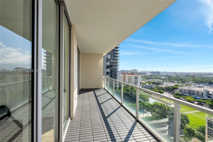 Covered balcony featuring dark-toned tiled flooring, glass-paneled railing, and expansive floor-to-ceiling sliding glass doors