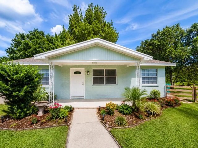 Mint green brick exterior featuring a covered front porch, white entry door, and a concrete walkway