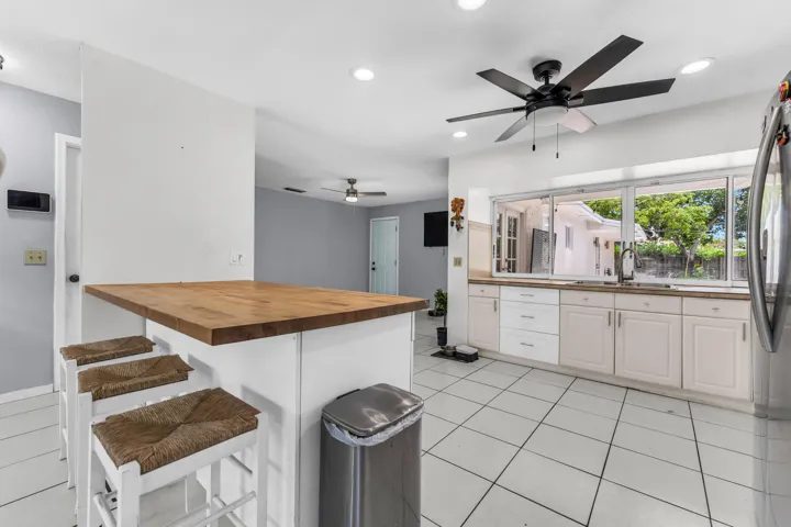 Kitchen featuring a butcher block peninsula, white cabinetry, integrated sink, tile flooring, and a ceiling fan