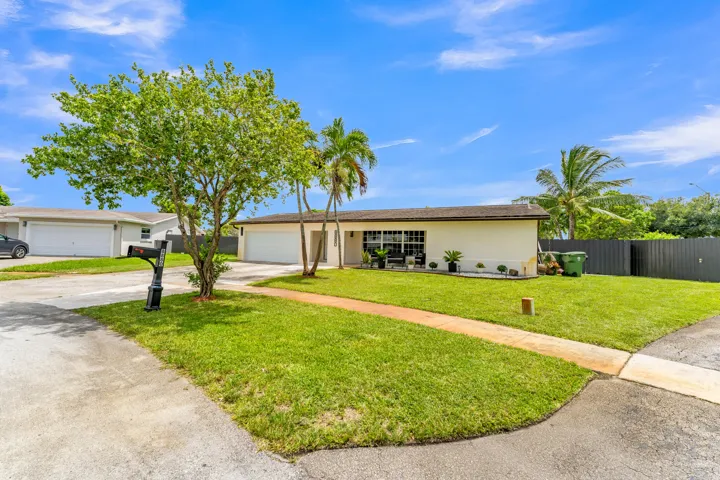 Single-story residence featuring a two-car garage, expansive front lawn, and mature palm trees