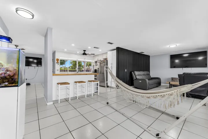 Open-concept living space featuring light tile flooring, a kitchen bar with a wood-finish countertop, white cabinetry, and recessed lighting