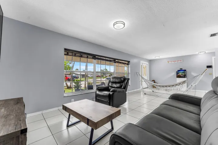 Spacious living area featuring large window, light-colored tile flooring, flush-mount lighting, and neutral wall tones