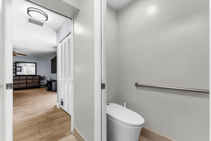 Private water closet featuring a modern toilet with integrated bidet functionality and a wall-mounted grab bar