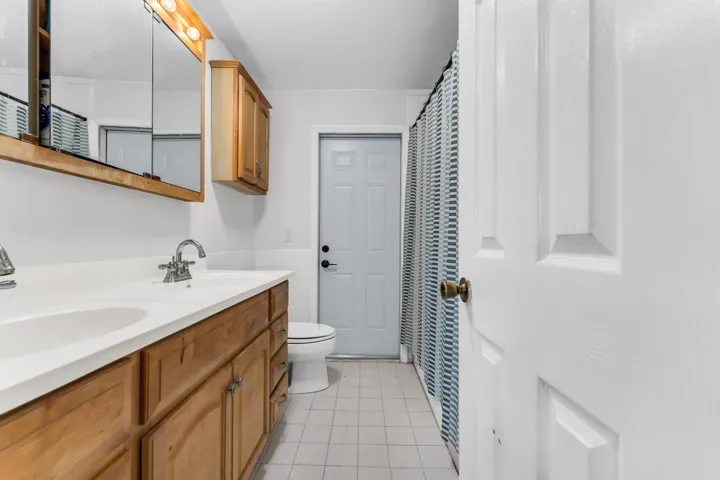 Bathroom featuring a dual-sink vanity with wood-finish cabinetry, a white countertop, and tiled flooring