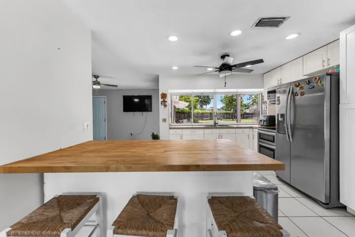 Kitchen featuring a wood-finish peninsula, stainless steel appliances, white cabinetry, recessed lighting, and a large window overlooking the backyard