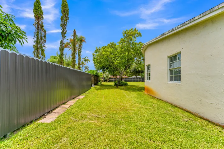 Expansive grassy yard featuring a tall metal privacy fence, mature trees, and a stucco exterior with multiple windows