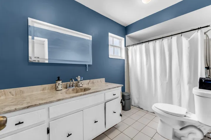 Bathroom located in 2nd primary bedroom featuring a vanity with a light-toned stone countertop, white cabinetry with black hardware, and a framed mirror
